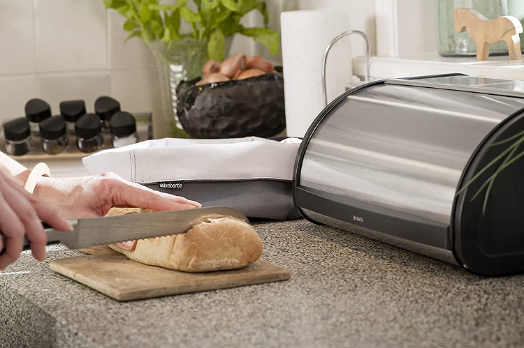 person slicing loaf of bread in front of stainless steel bread box