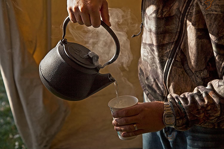 person pouring hot water into cup from cast iron teapot