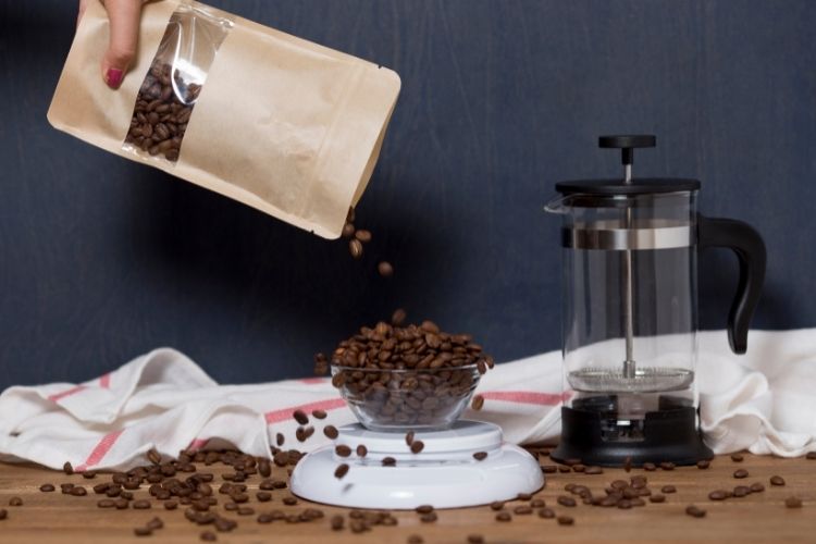 coffee beans pouring out of bag into bowl next to French Press Coffee Maker