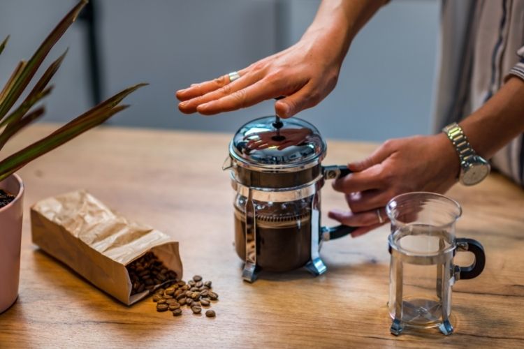 person using French Press Coffee ont able styled with coffee beans