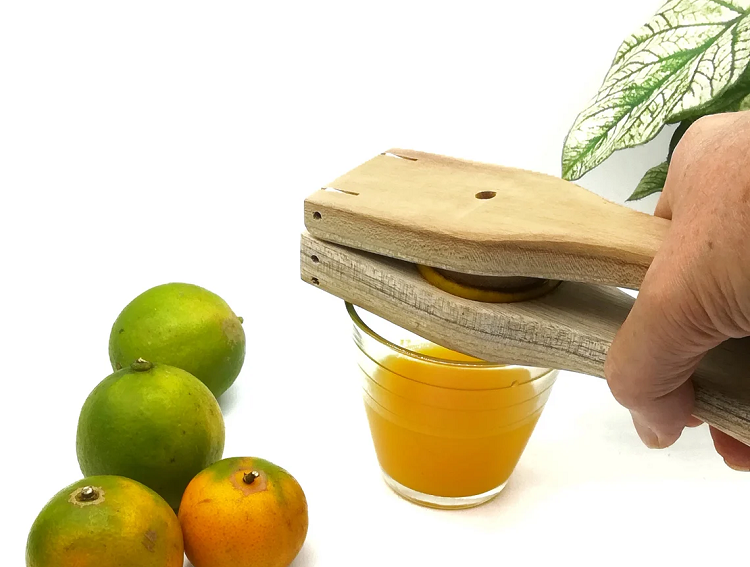 person squeezing citrus with wooden paddle lemon squeezer next to limes