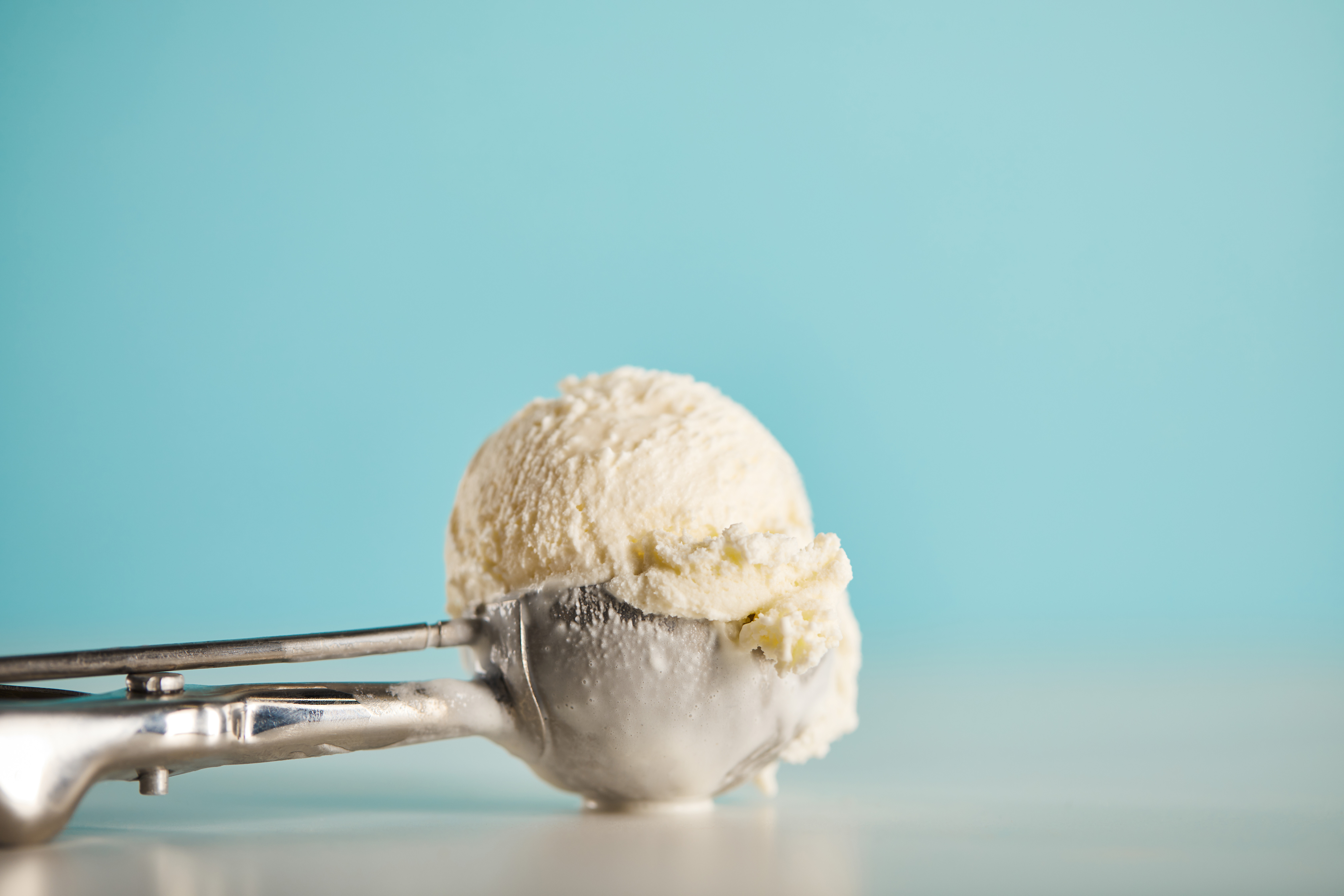 vanilla ice cream in ice cream scoop in front of blue wall