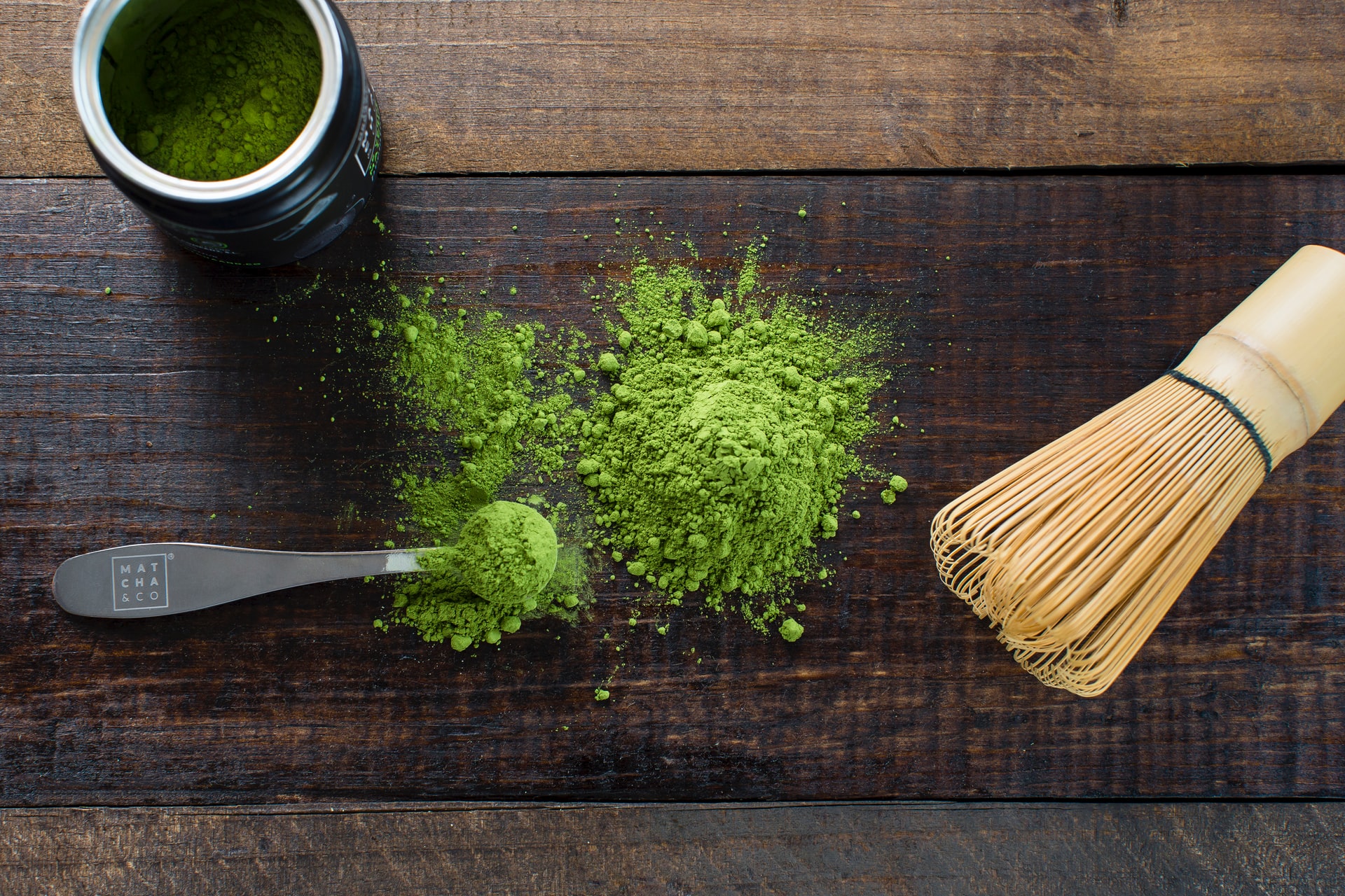 matcha green tea powder on tabletop with bamboo whisk and measuring spoon