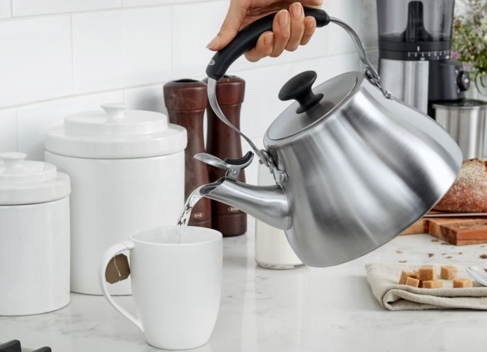 persons hand pouring water out of oxo tea kettle into white mug