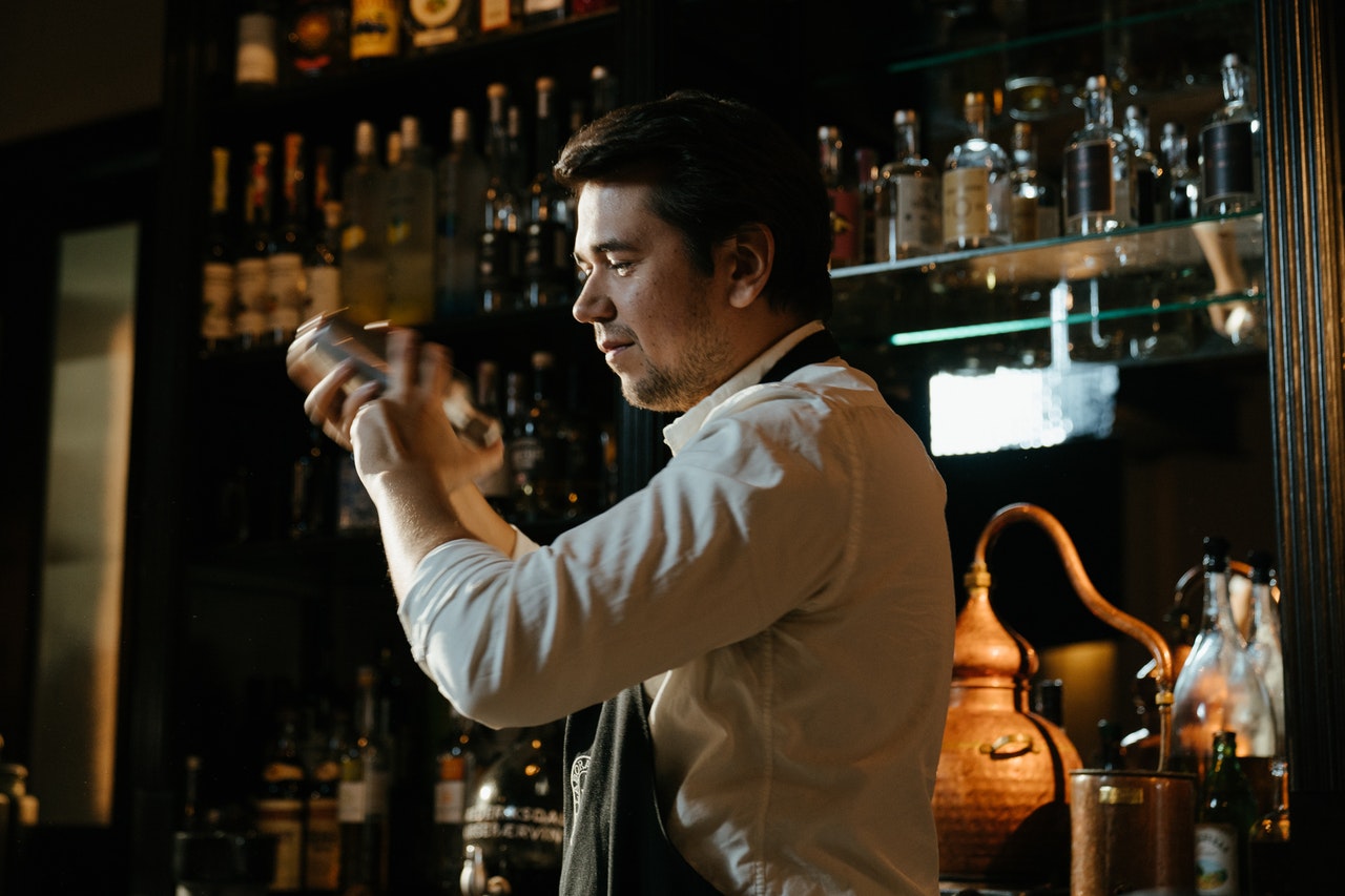 male bartender shaking cocktail saker behind bar