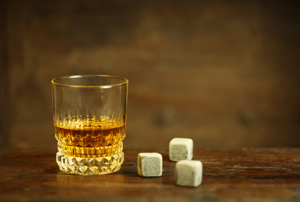 grey square whiskey stones next to glass of whiskey