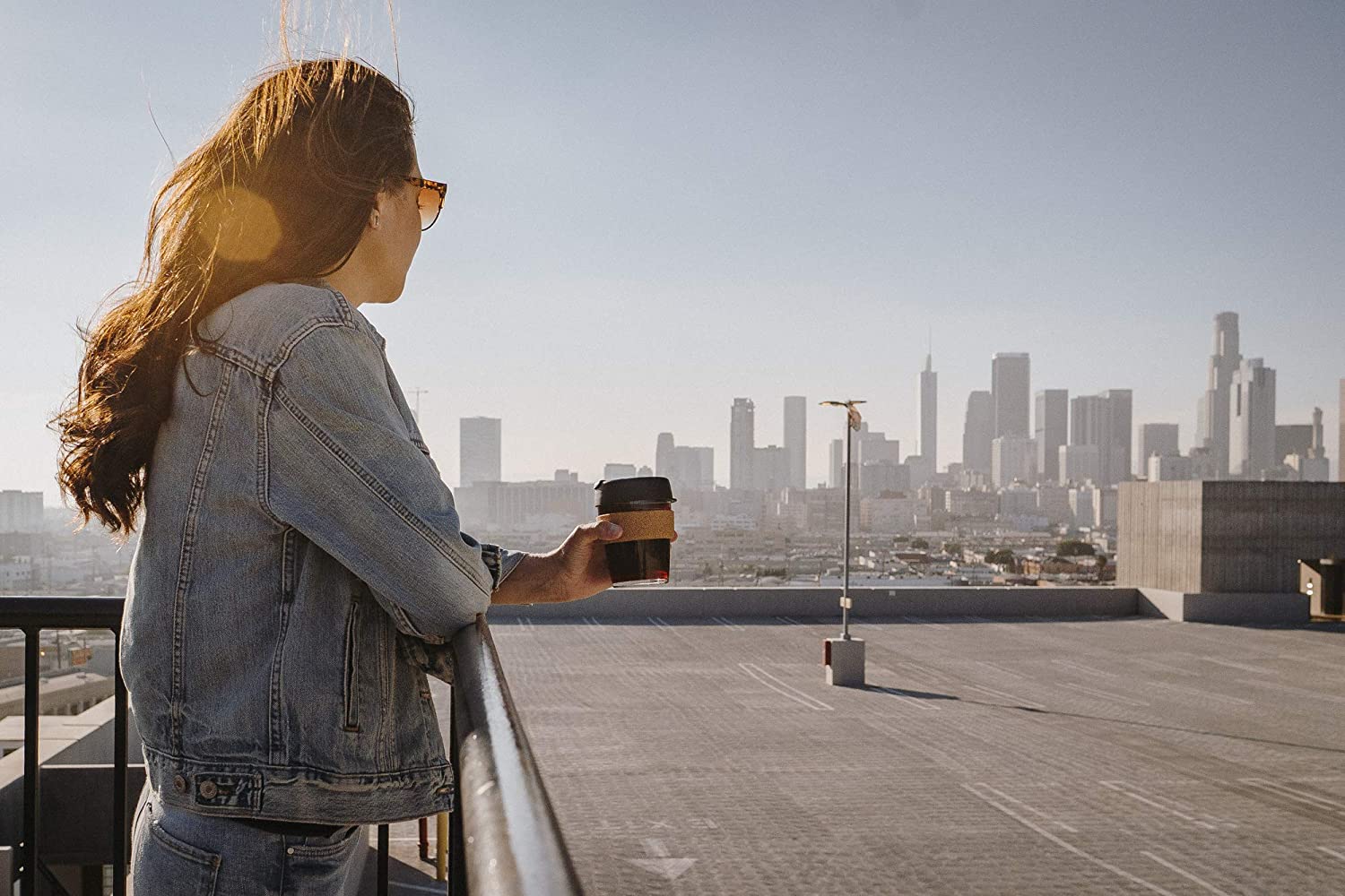 person on city rooftop holding travel coffee cup