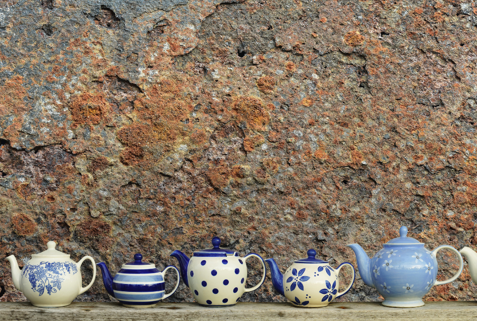 white and blue ceramic tea kettles in front of stone wall